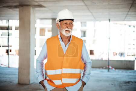 Photo for A senior construction site manager visually inspects a building project. Shot of a senior male foreman. A smiling, senior worker with a helmet takes a break from work. A senior worker - Royalty Free Image