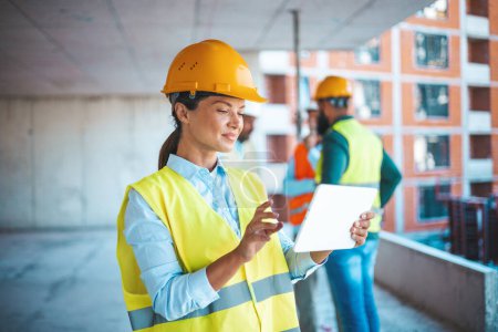 Photo for Beautiful mid adult woman architect wearing yellow hardhat at construction site while working on digital tablet. Supervisor wearing safety helmet while working in a building site. Successful and proud inspector looking away with copy space. - Royalty Free Image