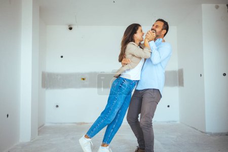 Téléchargez les photos : Couple dansant heureux avec appartement choix. Déménagement, immobilier, concept de loyer. Heureux et excité jeune couple regarder autour de lui dans l'émerveillement à leur nouvellement acheté - en image libre de droit