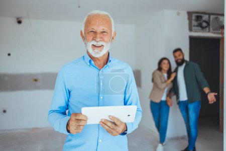 Photo for Male real estate agent holding a tablet and looking at camera smiling very happy. Happy real estate agent showing a house. Real estate agent at his work - Royalty Free Image