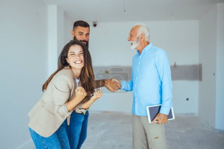 Photo for Real Estate Agent showing a house under construction to a couple and greeting them with a handshake at a construction site. Estate Agent Greeting Couple During Visit To New Home - Royalty Free Image