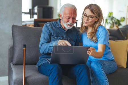 Photo for Active senior man using laptop with female carer sitting by on sofa at home. Nurse help senior man with internet and laptop on the sofa in a retirement home. Healthcare worker, caregiver or medical professional helping - Royalty Free Image