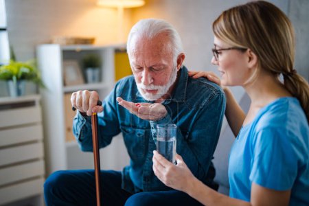 Photo for Nurse visiting mature patient at home. She is holding pill bottle and talking to patient how to use it. Home care for old people. Senior patient holds prescription and talks with smiling nurse - Royalty Free Image