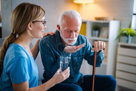 Photo for Senior male patient consult with physician nurse at nursing home. Caregiver therapist pharmacist girl hold medicine pills bottle, explain prescription to elderly old man in living room in house. - Royalty Free Image