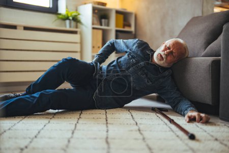 Photo for A Disabled Retiree with Walking Cane Fell on the Floor of the Living Room. Disabled Senior Man Lying On Carpet. Senior man in pain on the floor after a fall - Royalty Free Image