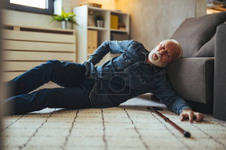 Photo for A Senior Man who is Using a Walking Stick is Lying on the Wooden Floor in his Apartment After he Fell in Serious Accident. Senior man lying on the floor of his room in an assisted living home - Royalty Free Image