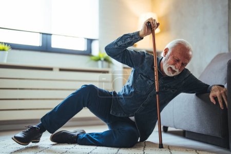 Photo for Elder senior man lying on floor after falling down with wooden walking stick beside couch on rug in living room at home. Old man suffering with pain and struggling to get up after falling down at home - Royalty Free Image