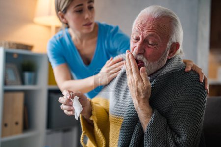 Photo for Nice senior bearded man taking a paper tissue, sick at home. Female caregiver helping senior man. Female professional doctor touching shoulder comforting upset senior patient. - Royalty Free Image