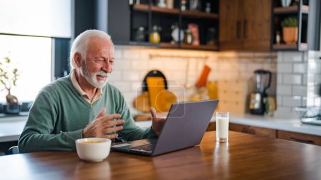 Photo for Good-looking enterpreneur working on laptop while having coffee and breakfast. Elderly man using laptop at kitchen table. Computer, money and communication with an elderly male pensioner in the kitchen - Royalty Free Image