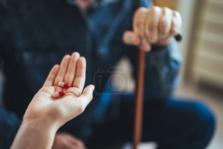 Photo for Female caregiver giving the medicine to her older male patient. Young female doctor visits a senior man and prescribes him medicine at home. Female nurse giving medication instructions to elderly patient - Royalty Free Image