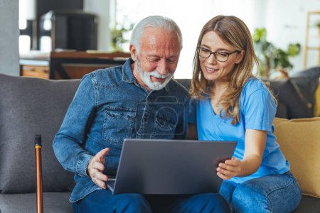 Photo for Active senior man using laptop with female carer sitting by on sofa at home. Nurse help senior man with internet and laptop on the sofa in a retirement home. Healthcare worker, caregiver or medical professional helping - Royalty Free Image