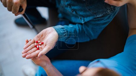 Photo for Female nurse sitting on bed and giving instructions to senior patient when to take his pills in nursing home. Daily Dose of Medication. Healthcare worker or caregiver visiting senior man indoors at home, explaining medicine dosage. - Royalty Free Image