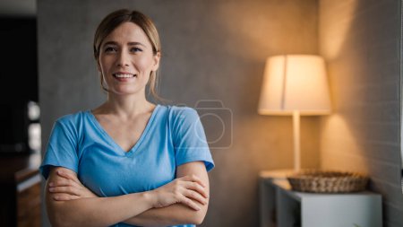 Photo for Smiling female nurse in medical scrubs. The career of nursing requires a lot of compassion. ortrait of Female nurse inside the modern penthouse apartment. Portrait of a home caregiver looking thoughtful and smiling - Royalty Free Image