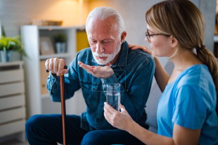 Photo for Female caregiver giving the medicine to her older male patient. Young female doctor visits a senior man and prescribes him medicine at home. Female nurse giving medication instructions to elderly patient - Royalty Free Image