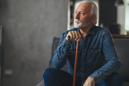 Photo for Grey hair man with disabled stick sitting on sofa and thinking at home - Royalty Free Image