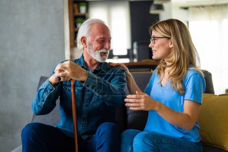 Photo for Young female nurse and senior man with disabled stick on sofa at home - Royalty Free Image