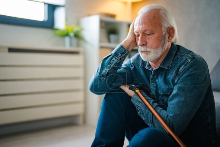 Photo for Sadness senior man with disabled stick sitting on floor near sofa at home - Royalty Free Image