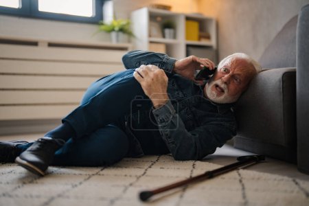 Photo for Mature caucasian man with painful lying on on floor and talking on smartphone near sofa at home - Royalty Free Image