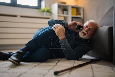Photo for Mature caucasian man with painful lying on on floor and talking on smartphone near sofa at home - Royalty Free Image