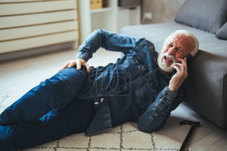 Téléchargez les photos : Homme caucasien mature avec douloureux couché sur le sol et parlant sur smartphone près du canapé à la maison - en image libre de droit