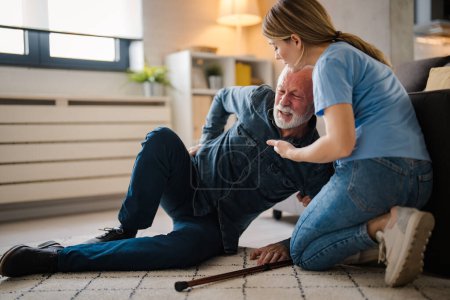 Photo for Young female nurse helping senior man standing up from floor at home - Royalty Free Image