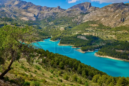 Landschaft des Guadalest-Stausees. Ruhige türkisfarbene See umgeben von felsigen Bergen mit grünen Bäumen vor blauem Himmel in der Natur von Guadalest in der Provinz Alicante in Spanien