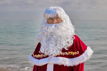Téléchargez les photos : Gros plan portrait du Père Noël sur fond de mer par une chaude journée d'été. Vacances de Noël ou du Nouvel An dans les pays chauds. Vacances d'été du Père Noël. - en image libre de droit