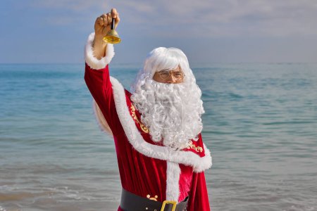 Téléchargez les photos : Le Père Noël saute sur la plage dans le contexte de la mer par une chaude journée d'été. Vacances de Noël ou du Nouvel An dans les pays chauds. Vacances d'été du Père Noël. - en image libre de droit