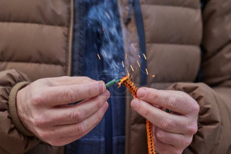 Primer plano de la mano del hombre encendiendo un petardo con mecha. Hombre sosteniendo un petardo ardiente en su mano.