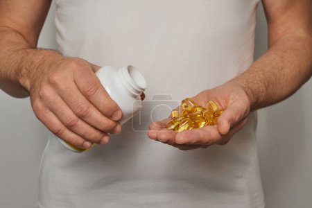 Un joven con una camiseta blanca le echa pastillas en la mano. Omega 3 cápsulas de aceite de pescado de oro. Primer plano sobre un fondo blanco.
