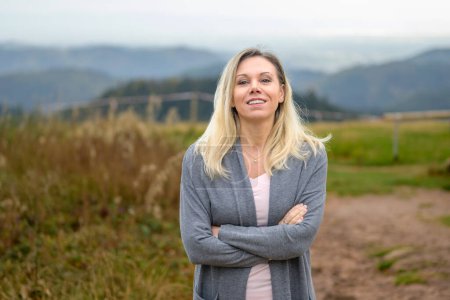 Photo for Beautiful gently smiling middle-aged blonde woman with crossed arms is standing on a mountain in the Black Forest - Royalty Free Image