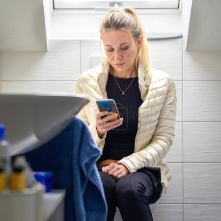 Photo for Attractive blonde woman holding a cellphone barely managed to use the bathroom due to diarrhea as she was about to go shopping - Royalty Free Image