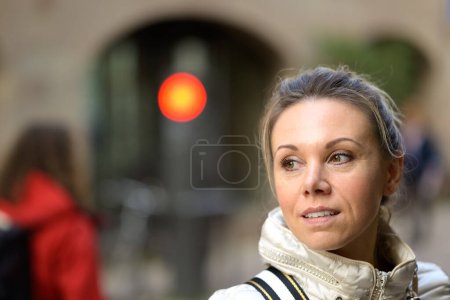 Foto de Retrato de una atractiva mujer de mediana edad suavemente sonriente con el pelo rubio y una cola de caballo parece interesado a un lado en una calle comercial con luz roja en el fondo - Imagen libre de derechos