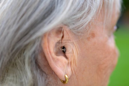 Foto de Elderly grey-haired deaf lady in her eighties with a hearing aid in her ear - Imagen libre de derechos
