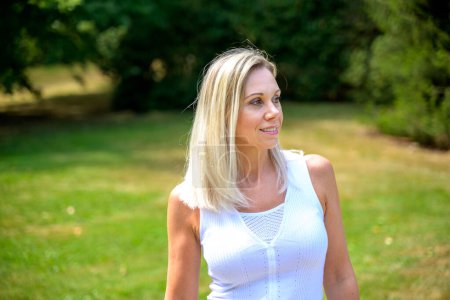 Photo for Attractive middle aged blond woman with long blond hair walking in a park in summer - Royalty Free Image