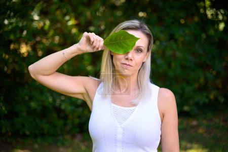 Photo for Attractive blond woman covering one eye with a green leaf in a conceptual image - Royalty Free Image