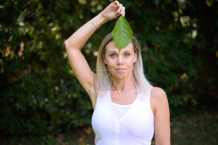 Photo for Attractive blond woman holding a green leaf to her forehead in a wellness, spa or eco concept - Royalty Free Image