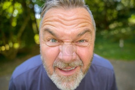 Foto de Hombre barbudo mayor mirando dentro de la lente entrecerrando los ojos en un primer plano de la cabeza al aire libre - Imagen libre de derechos