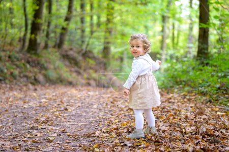 Photo for Full length shot of a little smiling girl turning around in the forest in autumn - Royalty Free Image