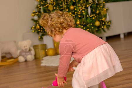 Téléchargez les photos : Petite fille joue avec son cadeau devant le sapin de Noël décoré à Noël - en image libre de droit