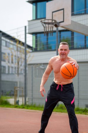 Photo for Middle age shirtless man in black sports shorts dribbles and looking to the camera on a sports field - Royalty Free Image