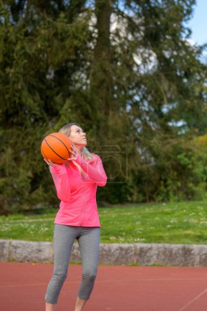 Foto de Atractiva mujer rubia a punto de saltar con el baloncesto en sus manos en un campo de deportes - Imagen libre de derechos