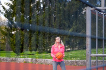 Foto de Atractiva mujer rubia sosteniendo el baloncesto en sus manos y mirando concentrada a la cámara en un campo deportivo - Imagen libre de derechos