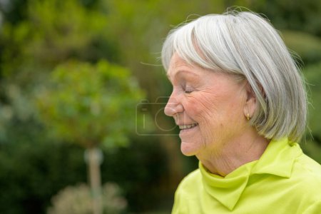 Téléchargez les photos : Dame âgée dans ses années 80 avec des cheveux blancs gris et une chemise verte a la tête sur le côté avec les yeux fermés - en image libre de droit