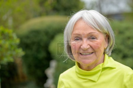 Téléchargez les photos : Femme âgée dans les années 80 avec des cheveux blancs-gris et une chemise verte sourit bien à la caméra - en image libre de droit