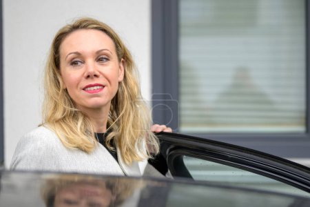 Téléchargez les photos : Femme d'âge moyen regarde de côté tout en entrant dans la voiture - en image libre de droit