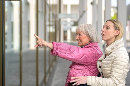 Photo for Side view of a mother and daughter standing and pointing to a shopping window - Royalty Free Image