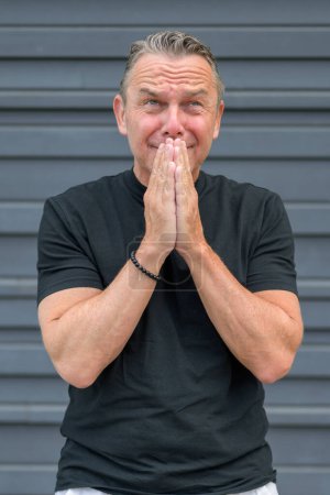 Photo for Three quarter length portrait of a distressed elderly man with both hands to his mouth in front of a blue wall - Royalty Free Image