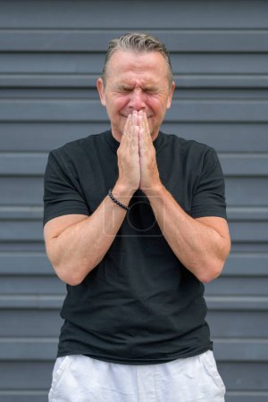 Photo for Three quarter length portrait of a distressed elderly man with both hands to his mouth in front of a blue wall - Royalty Free Image