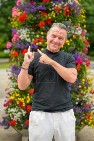 Foto de Retrato de tres cuartos de largo de un atractivo hombre mayor señalando sus dedos hacia una gran torre de flores - Imagen libre de derechos
